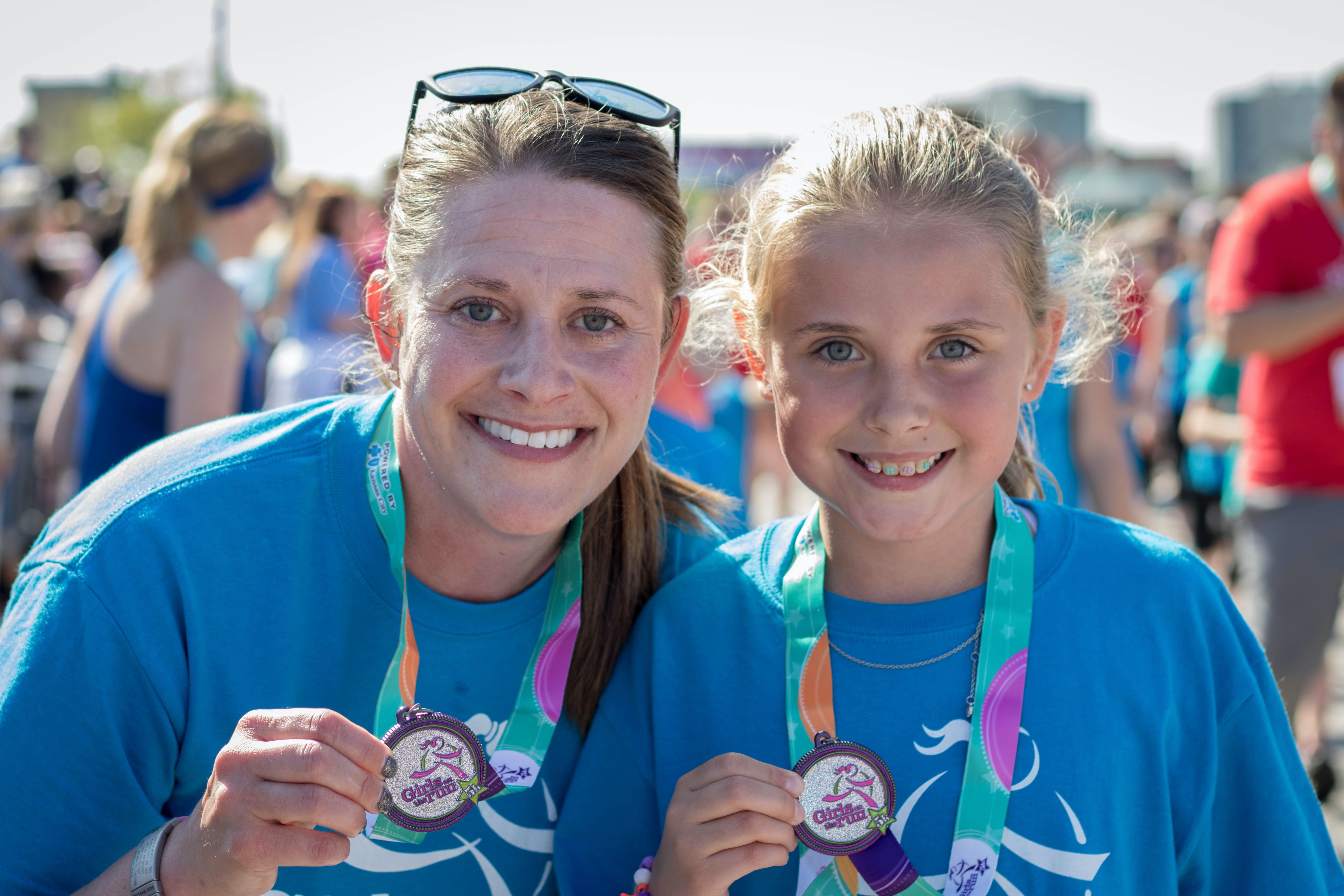 Girls on the Run participant holding program 5K medal with coach.